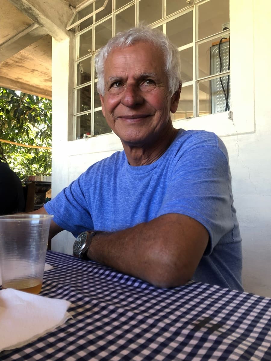 Don Zefe, de pelo blanco y playera azul, sonríe sentado a la mesa